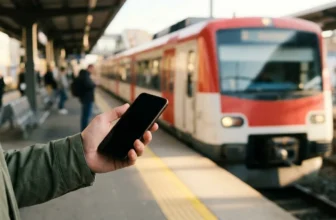 Hand mit Smartphone auf einem Bahnsteig vor einfahrender Regionalbahn